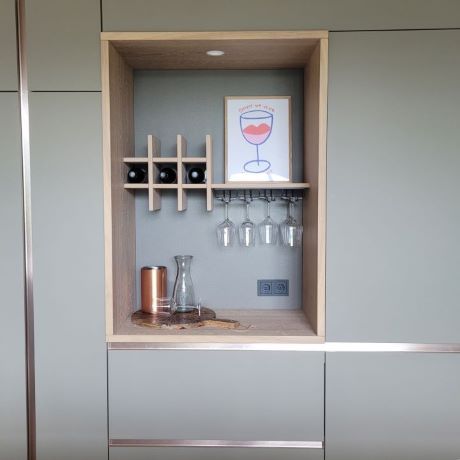 Nis in luxe maatwerkkeuken. Eiken handgemaakte wijnrek met hangende glazen. Matte fronten en messing greeplijsten